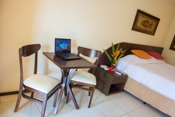 Habitación de hotel con cama, escritorio con una computadora portátil, dos sillas, mesita de noche con teléfono y un cuadro de peces colgado en la pared.