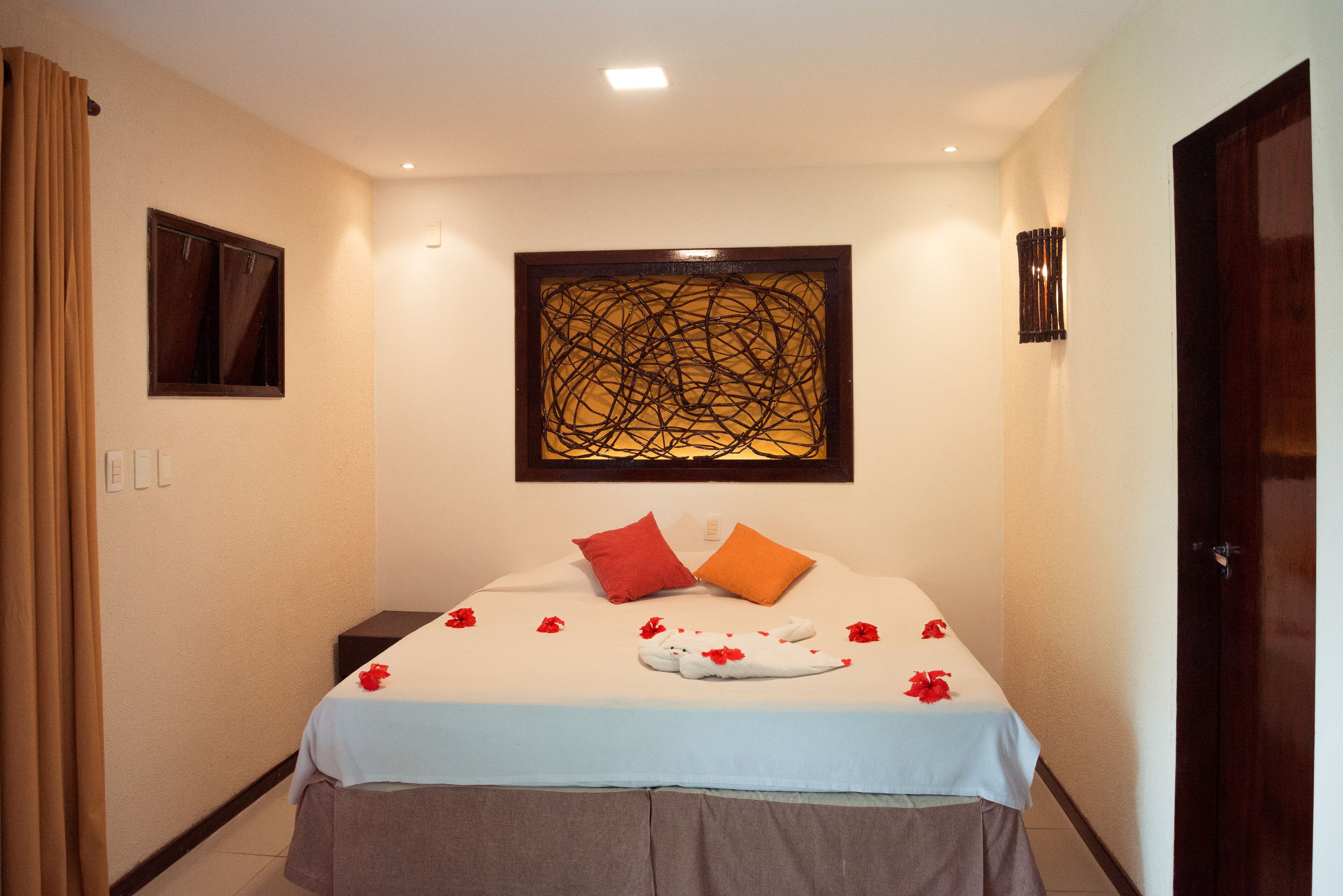 A hotel room with a bed, a window, a wall art piece, and a door.