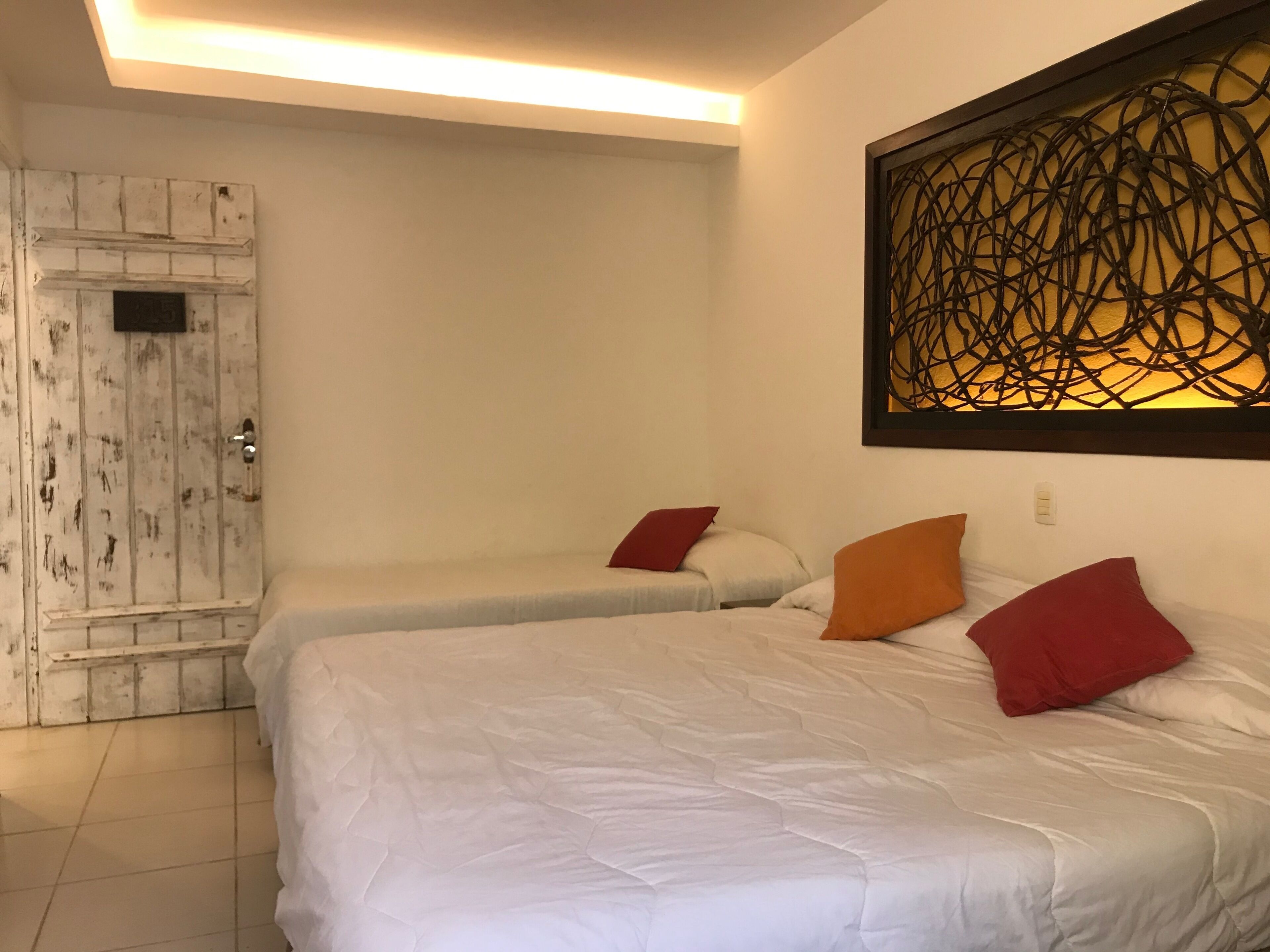 A hotel room with two beds, a wooden door, and a decorative wall piece.