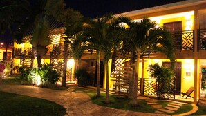 A hotel with a well-lit entrance, palm trees, and a stone pathway leading to the building. - Hotel Aconchego Porto de Galinhas (Ipojuca)