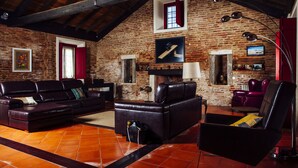 A rustic living room with exposed brick walls, leather sofas, and a fireplace. - Quinta da Gafaria (Almeirim)