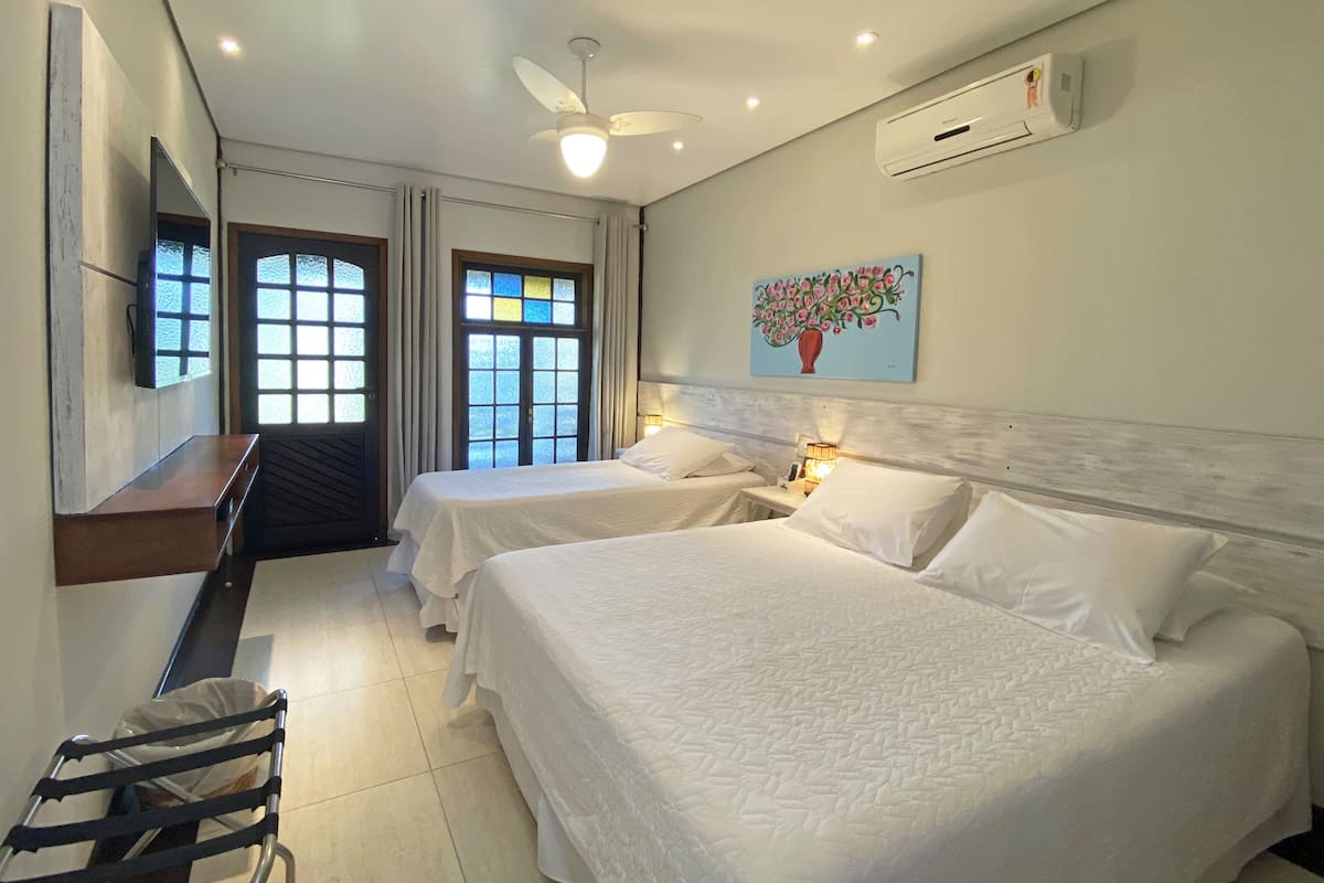 Une chambre d’hôtel avec deux lits, un bureau, une chaise, un ventilateur de plafond et un appareil de climatisation.