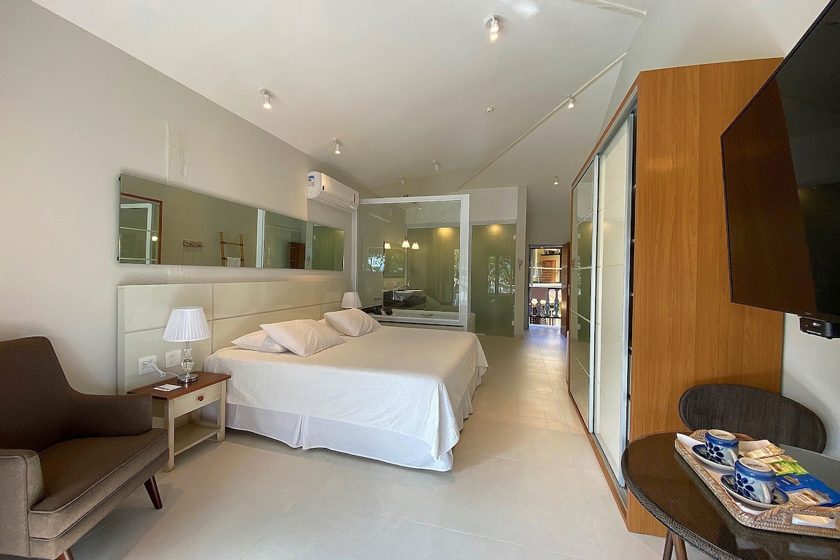 Une chambre d'hôtel moderne dotée d'un grand lit, de tables de chevet, d'une télévision et d'un coin salon avec un plateau contenant divers éléments pour le petit-déjeuner.
