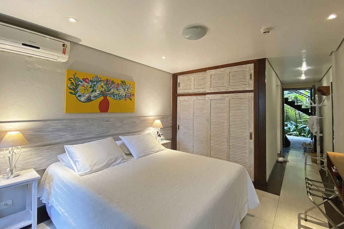 Une chambre à coucher comprenant un lit, des lampes de chevet, un climatiseur fixé au mur, un tableau et une armoire avec des portes coulissantes.