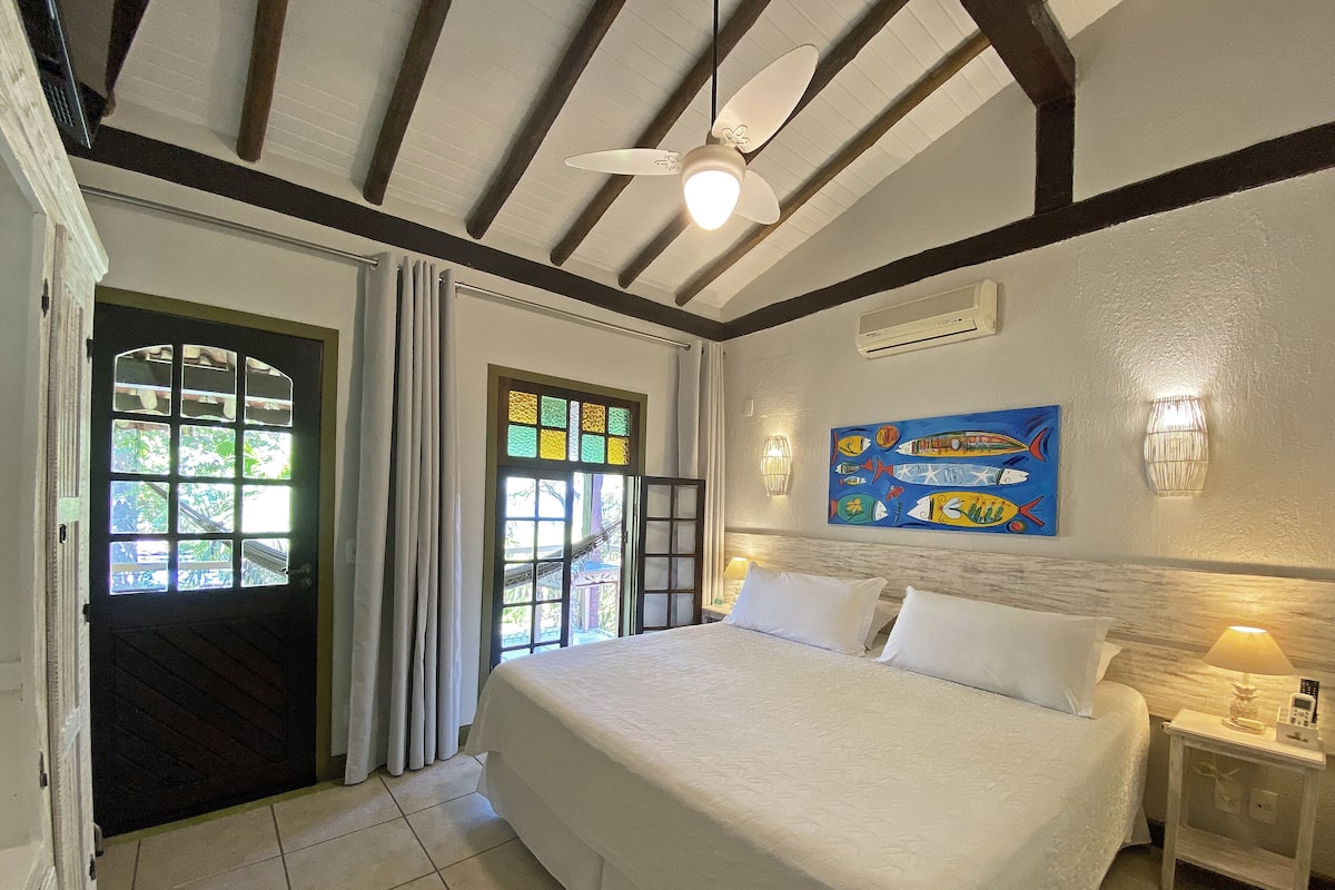 Une chambre à coucher avec un lit, un ventilateur de plafond, un tableau et une fenêtre avec des rideaux.