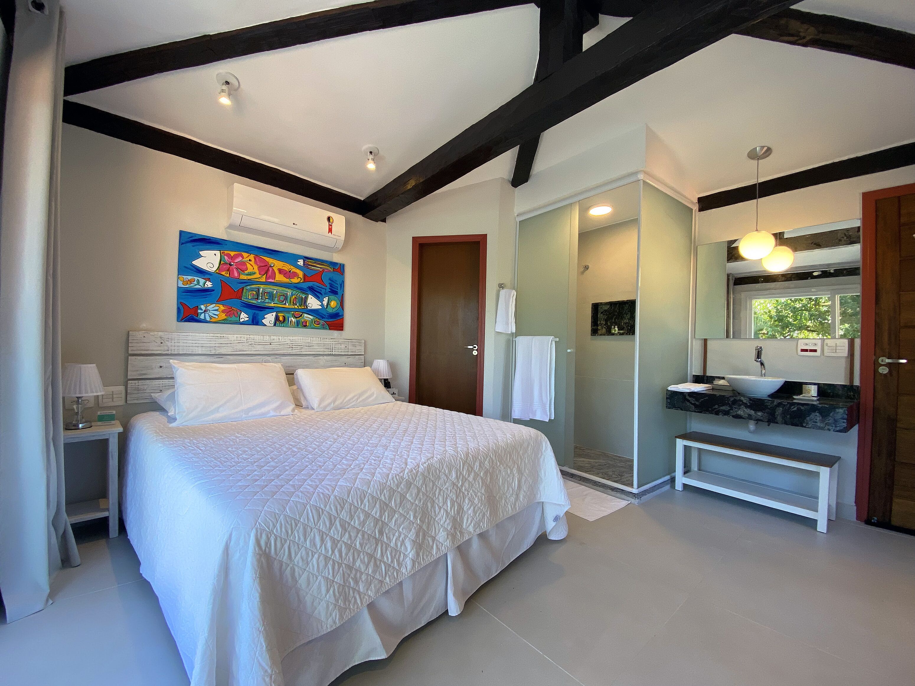 A bedroom with a large bed, a bathroom with a sink and mirror, and a colorful artwork on the wall.