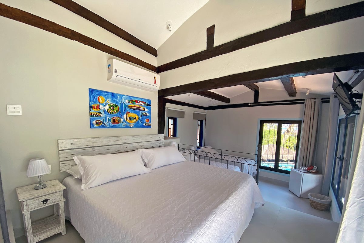 Une chambre à coucher avec un grand lit, une table de chevet, un climatiseur fixé au mur et un tableau coloré représentant des poissons.