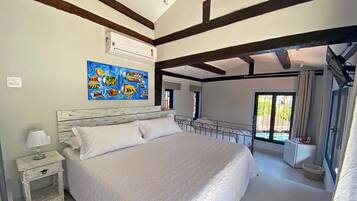 A bedroom with a large bed, a nightstand, a wall-mounted air conditioner, and a colorful fish painting.