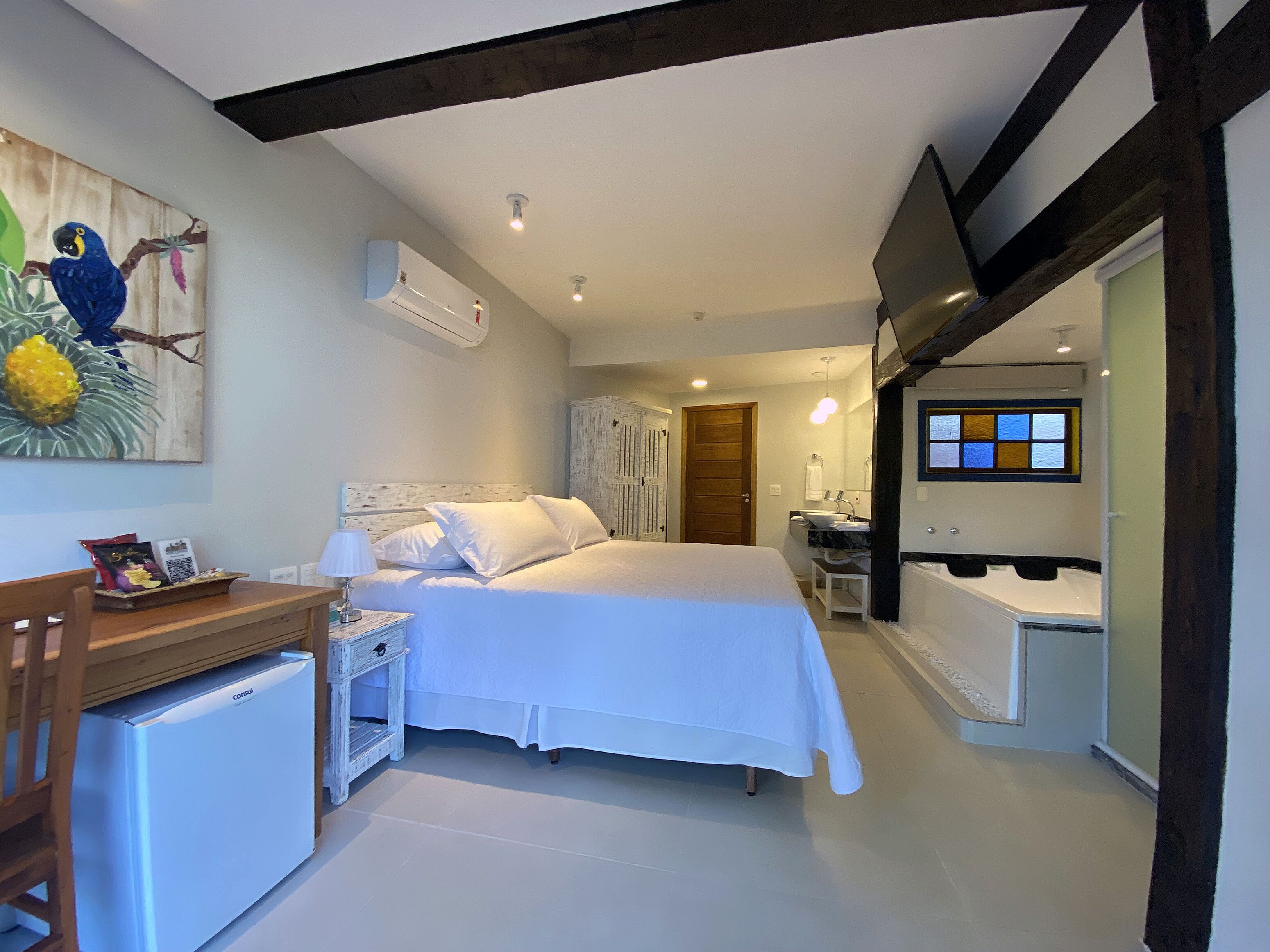 Un dormitorio con cama, mesita de noche, lámpara y un refrigerador pequeño. Incluye un baño con bañera y lavamanos.