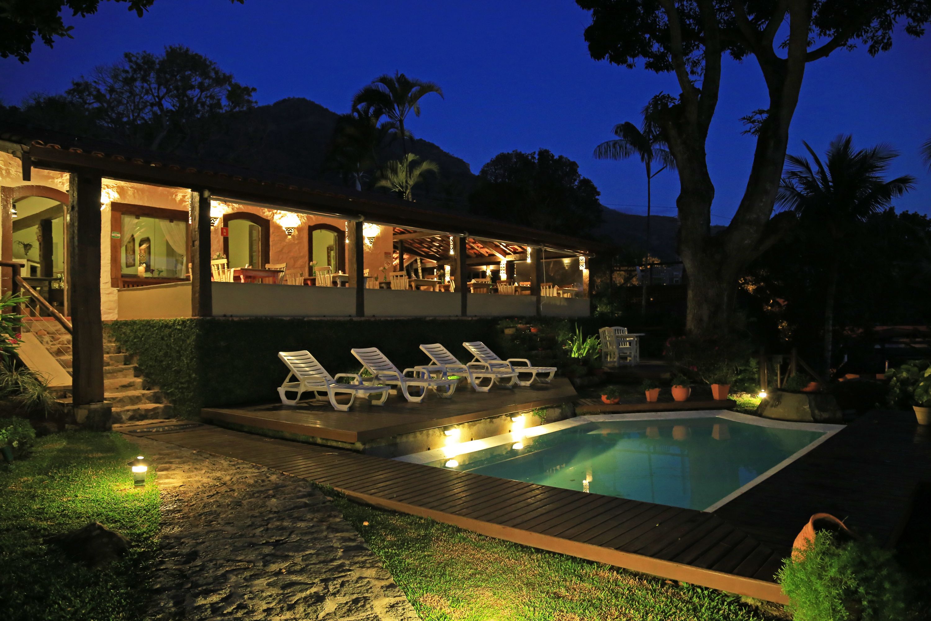 A poolside area with lounge chairs, a wooden deck, and a pool at dusk.
