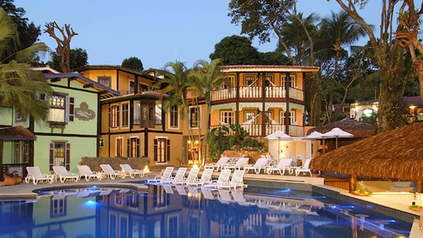 A swimming pool with lounge chairs and a thatched-roof structure. - Porto Pacuiba Hotel Ilhabela (Ilhabela)