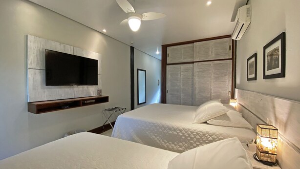 A hotel room with two beds, a TV mounted on the wall, a ceiling fan, and an air conditioning unit.