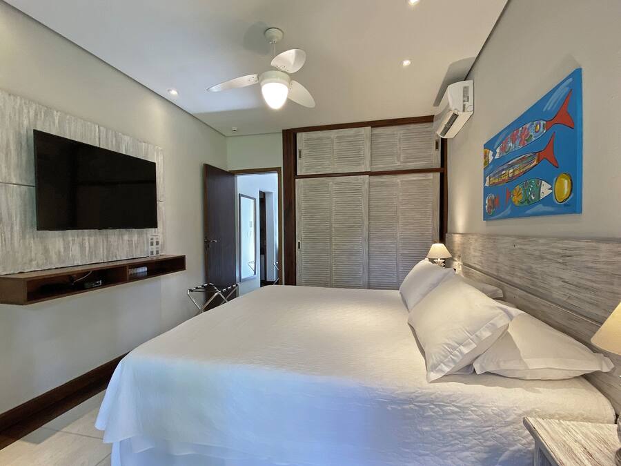 A hotel room with a large bed, a ceiling fan, a mounted TV, and a wall with a colorful fish painting.