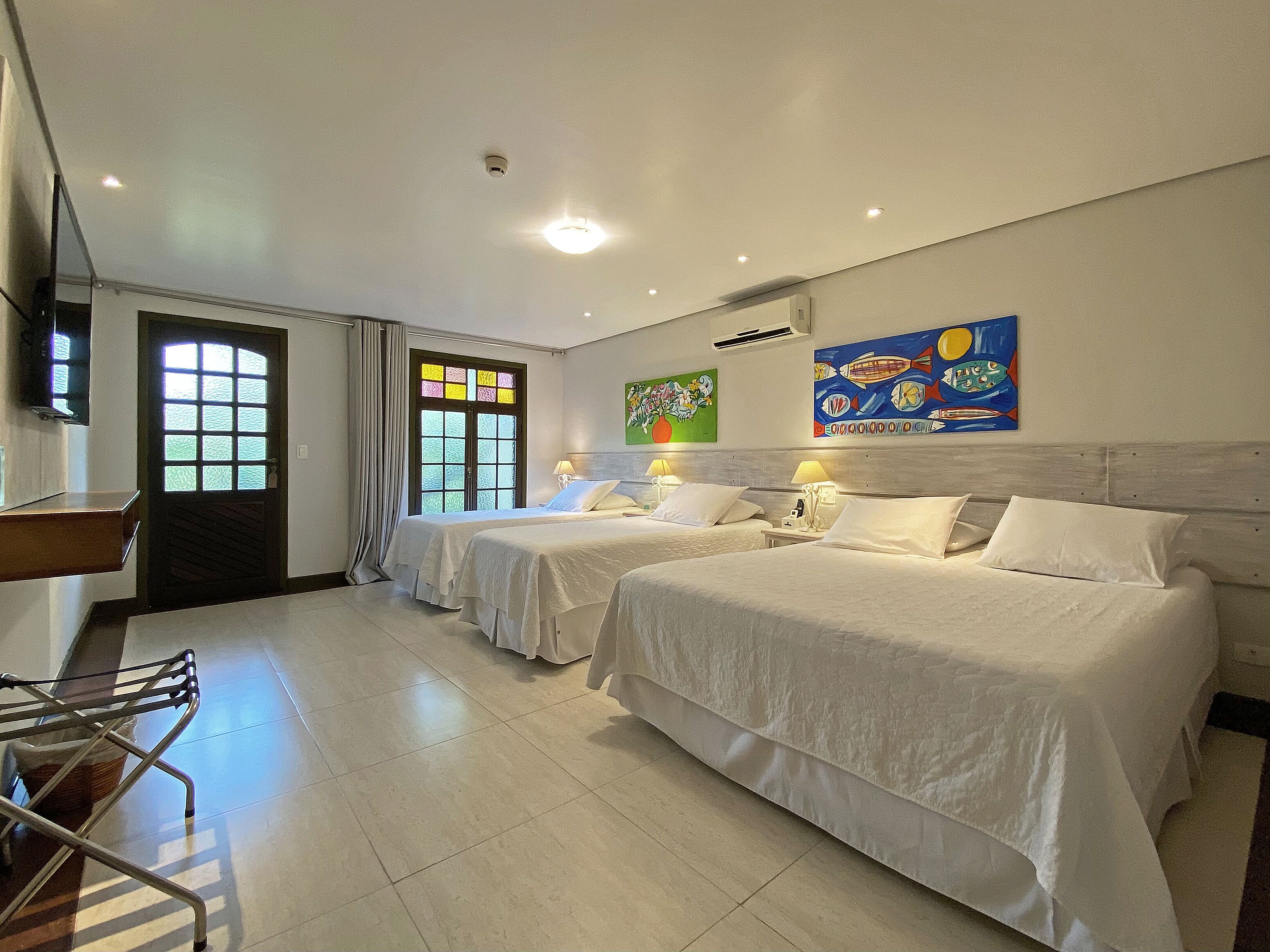 A hotel room with two beds, a TV, a window with curtains, and artwork on the wall.