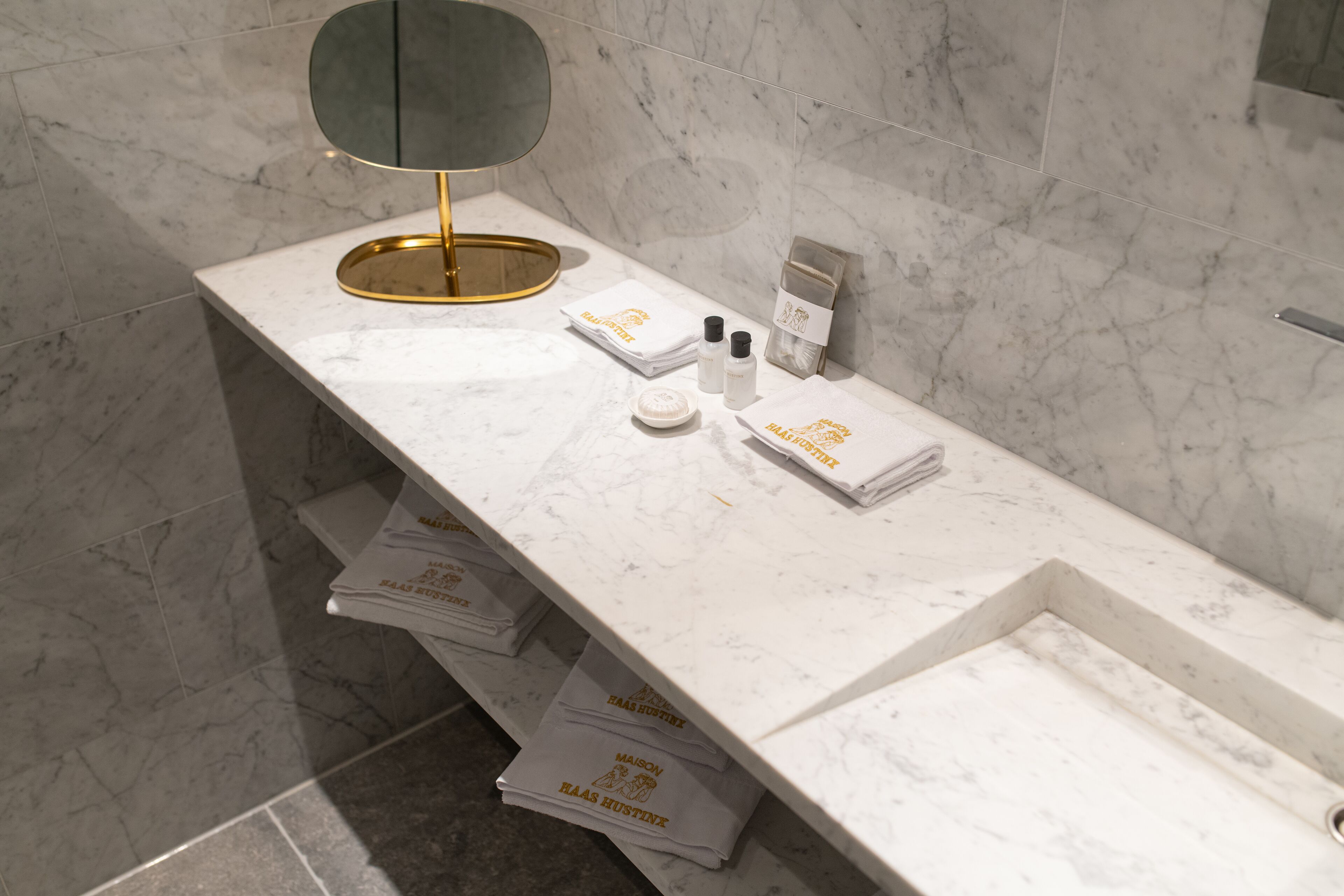 Une salle de bain moderne avec un comptoir en marbre, un miroir encadré d’or et des articles de toilette rangés avec soin.