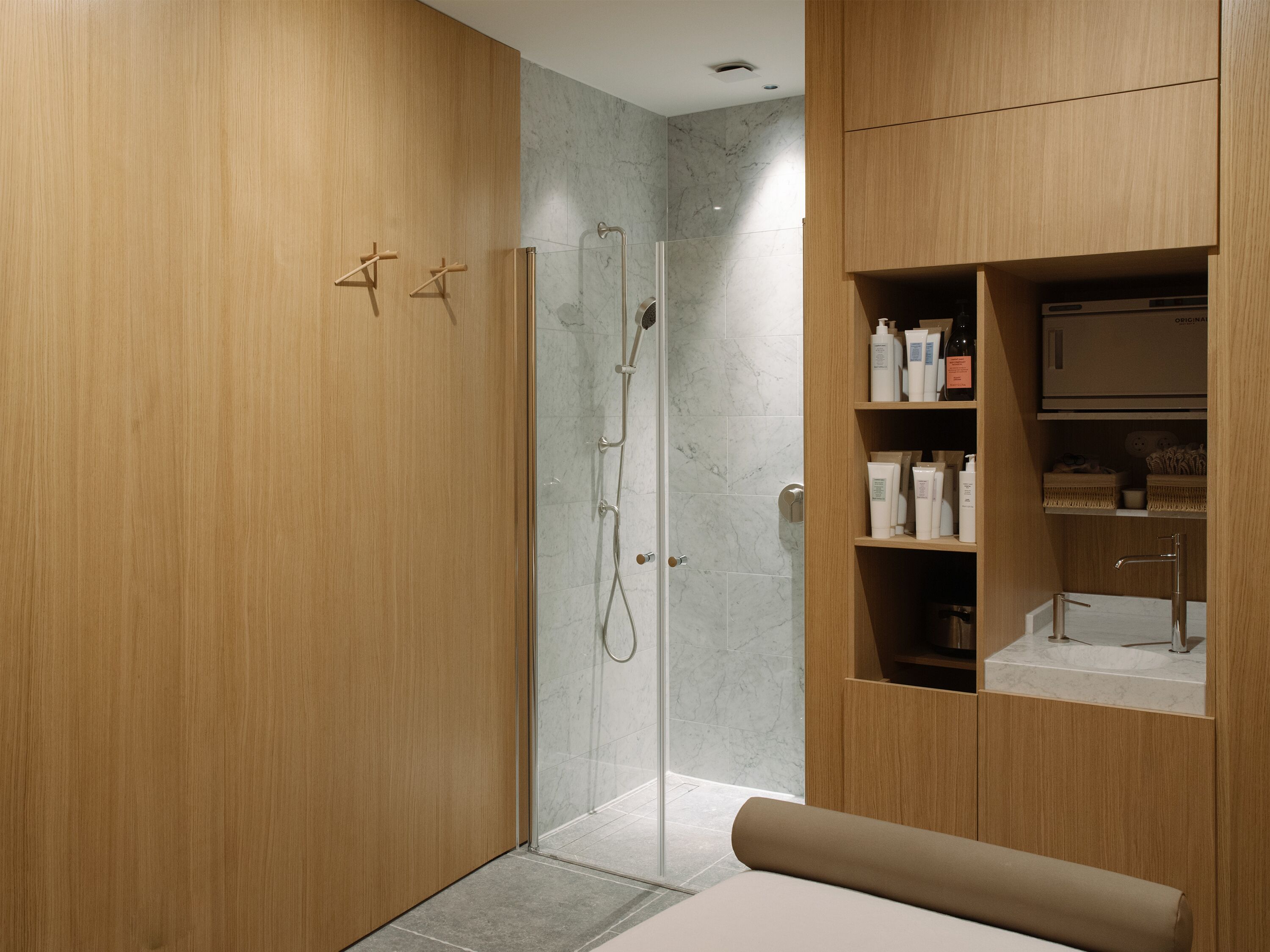 Een moderne badkamer met een houten wastafelmeubel, een glazen douchecabine en een inbouwkastje met toiletartikelen.