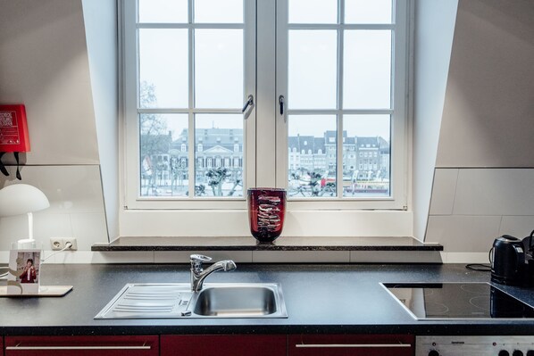 Una cocina con ventana, un lavamanos, una estufa y un florero rojo en el alféizar.