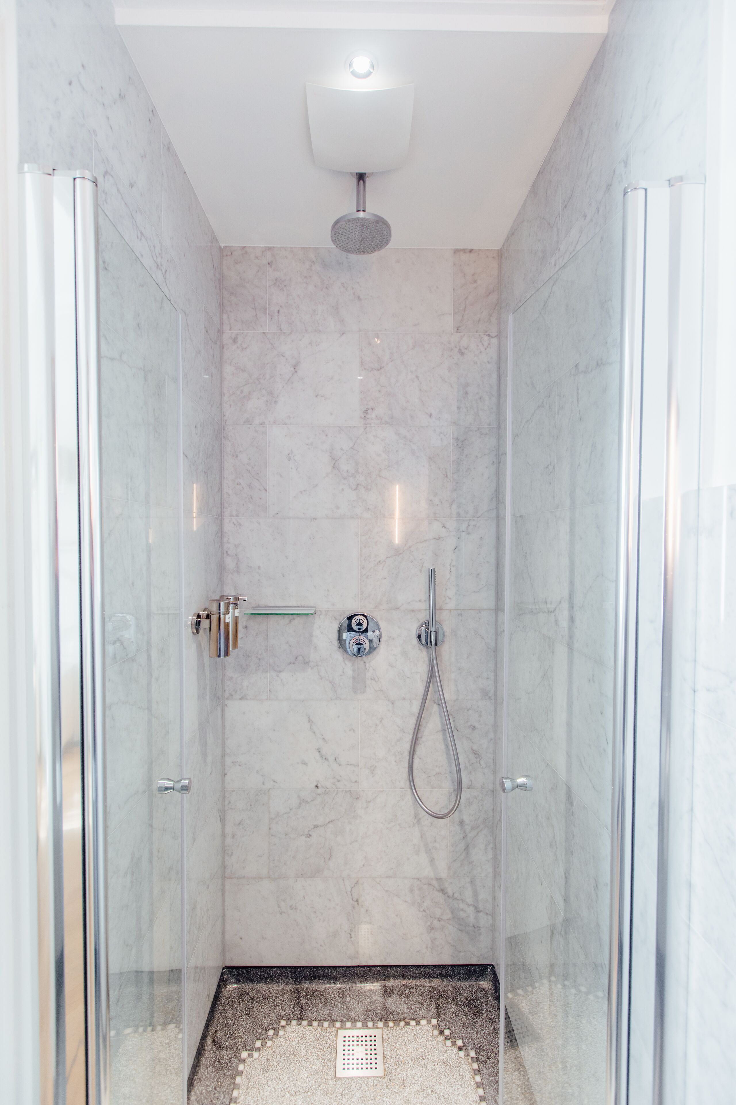 A modern shower with a glass door, a handheld showerhead, and a control panel.