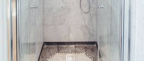 A modern shower with a glass door, a handheld showerhead, and a control panel.
