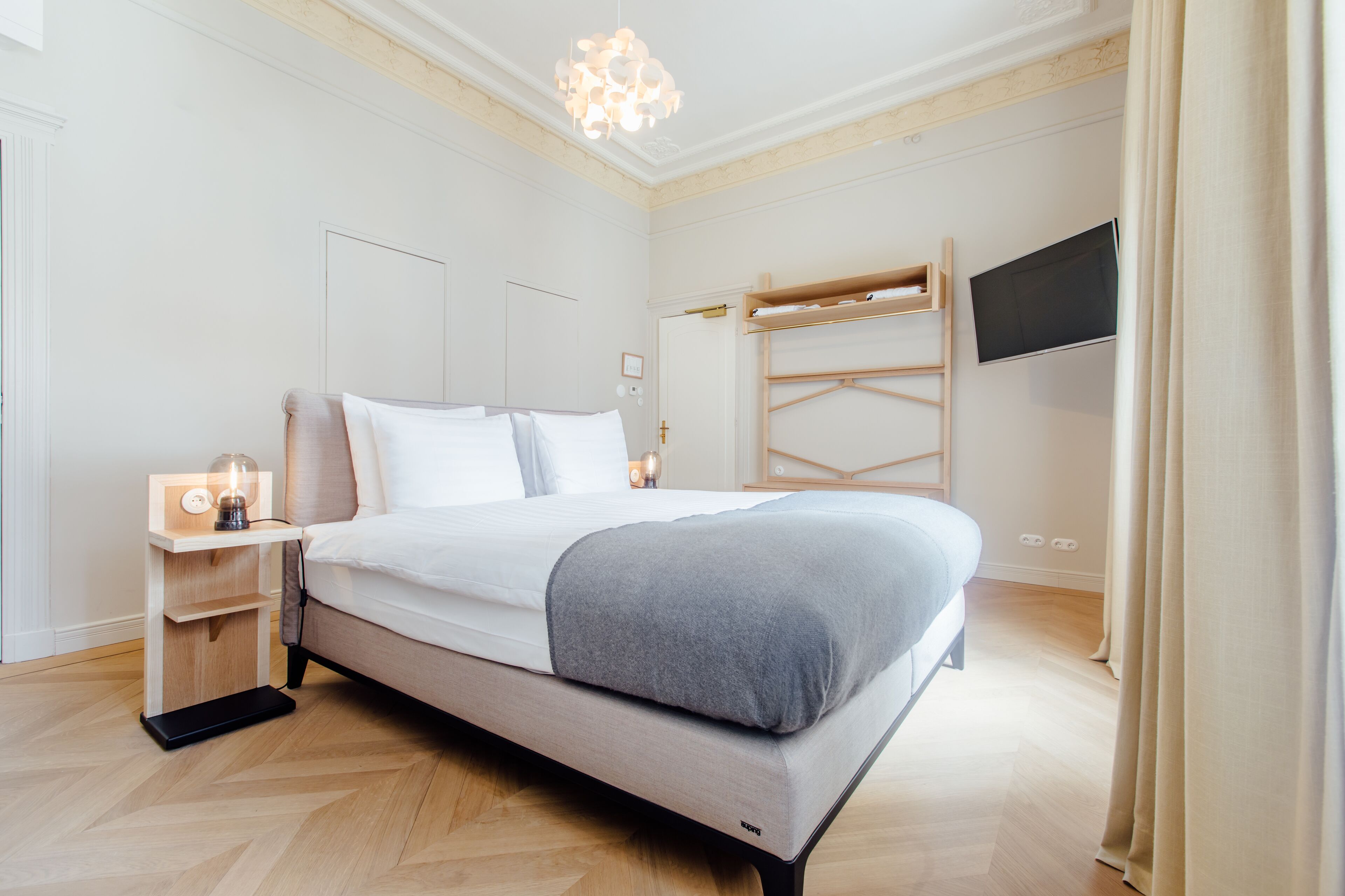 A modern bedroom with a bed, bedside tables, a TV, and a wooden bunk bed.