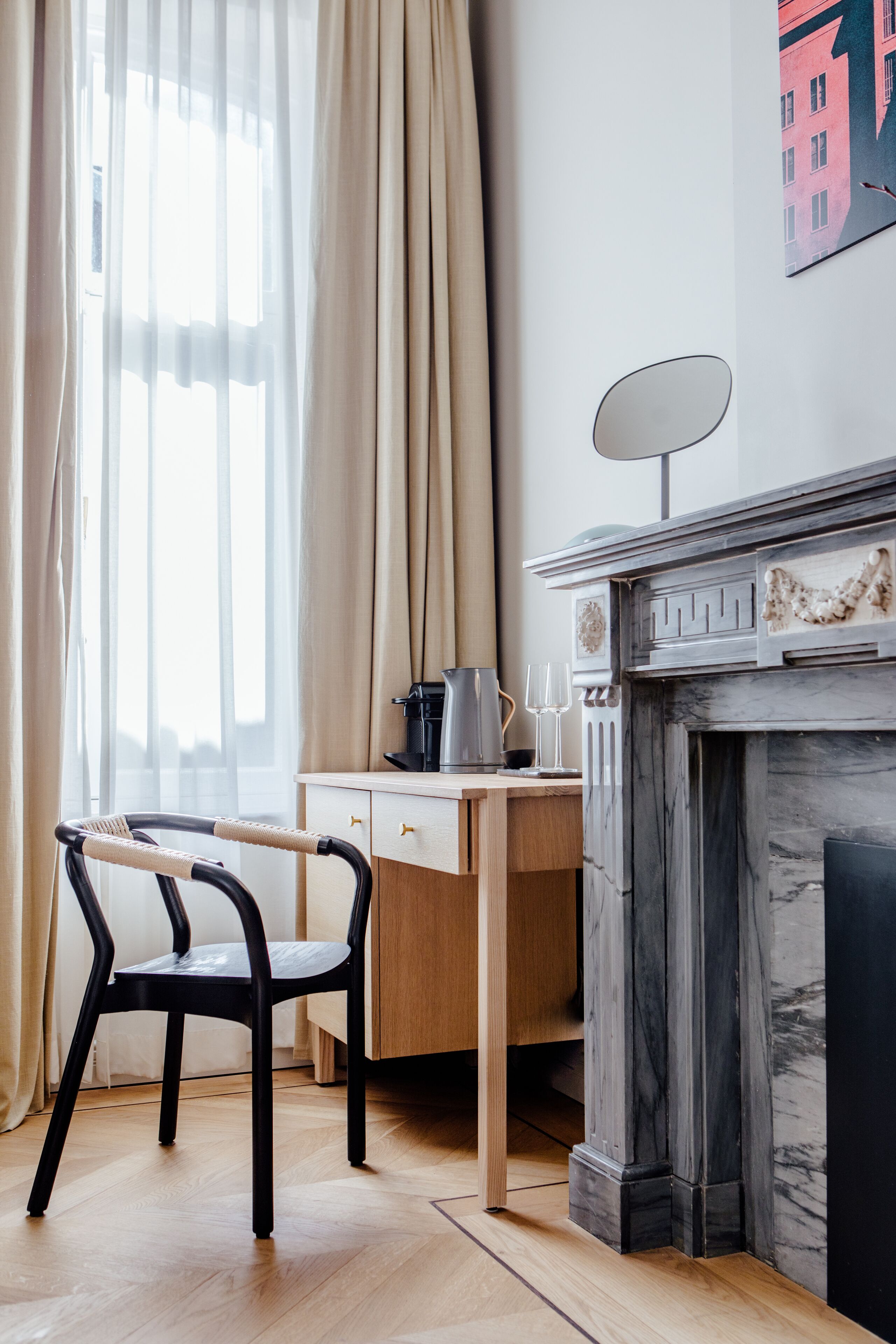 A room with a wooden desk, a chair, a fireplace, and a window with curtains.