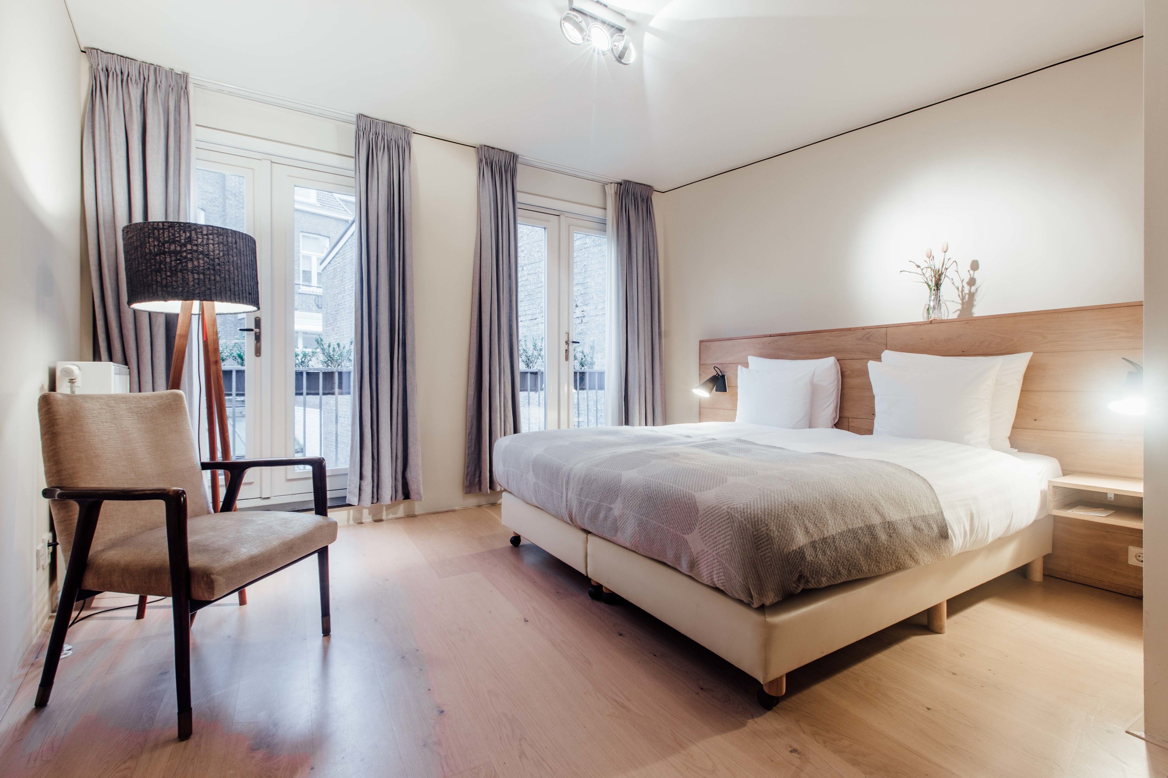 A modern bedroom with a large bed, a chair, a floor lamp, and a view of the outside.