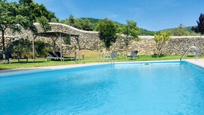 Ein klares, blaues Schwimmbecken mit Liegestühlen und einer Steinmauer im Hintergrund.