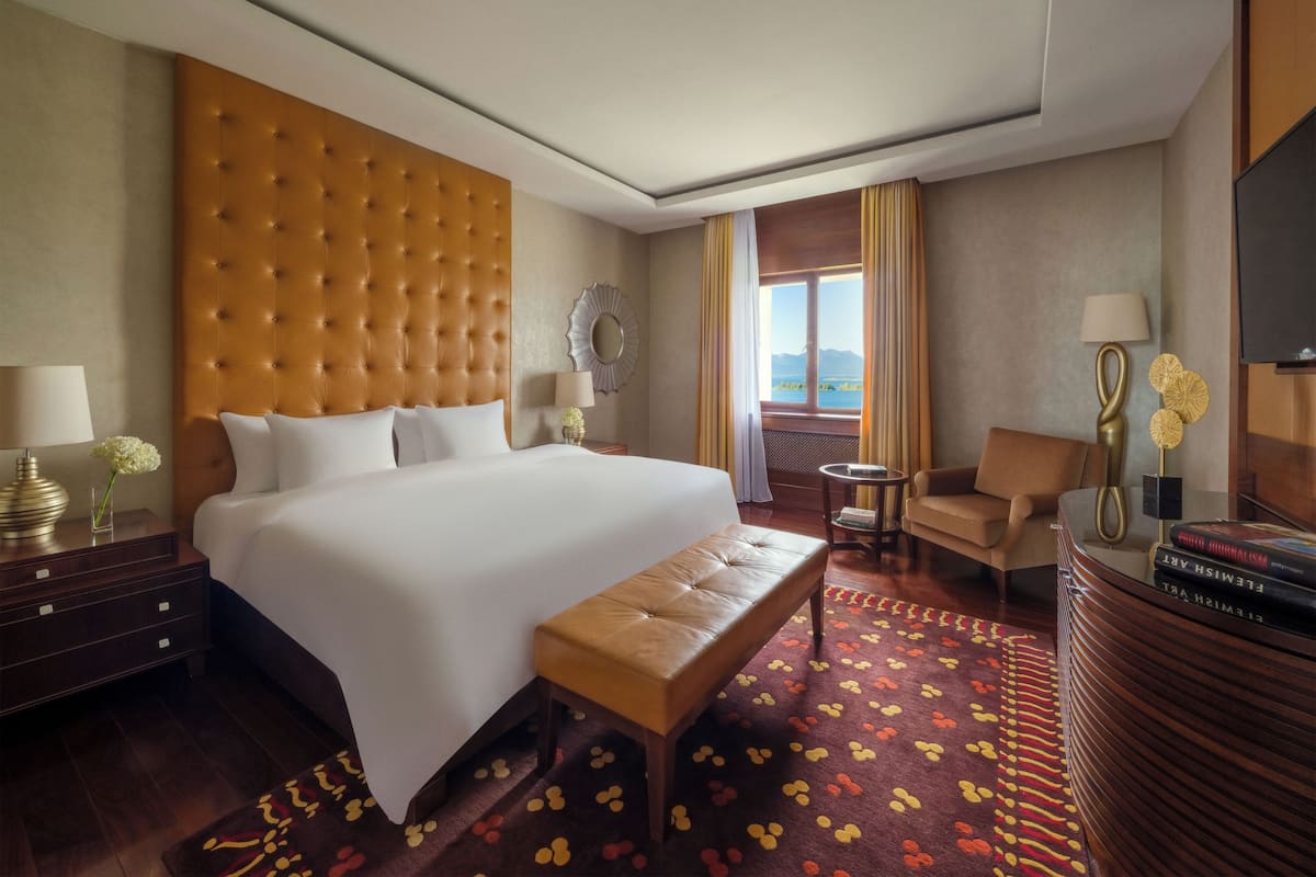 Una habitación de hotel con una cama grande, una zona de estar con una silla, una mesita y un televisor.