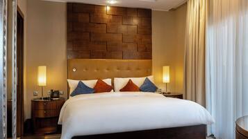 A hotel room with a large bed, a wooden headboard, two bedside lamps, and a view of a curtain.