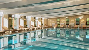 A large indoor swimming pool with multiple lounge areas and sunbeds, surrounded by large windows and a tiled wall. - Rixos Borovoe (Burabay)