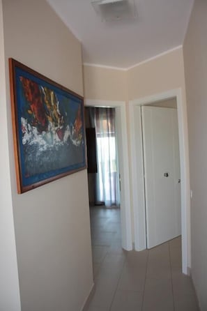 A hallway with a large abstract painting on the left, a white door on the right, and a view into another room through a glass door. - Case Vacanze Bellavista (Porto Empedocle)