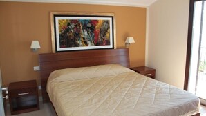 Een slaapkamer met een groot bed, een houten hoofdbord, twee nachtkastjes met lampen, en een kleurrijk abstract schilderij aan de muur.