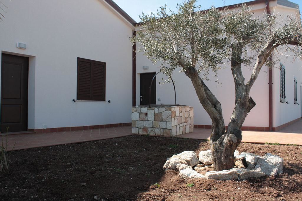 Un bâtiment à la façade blanche, avec un banc en pierre et un arbre dans la cour.