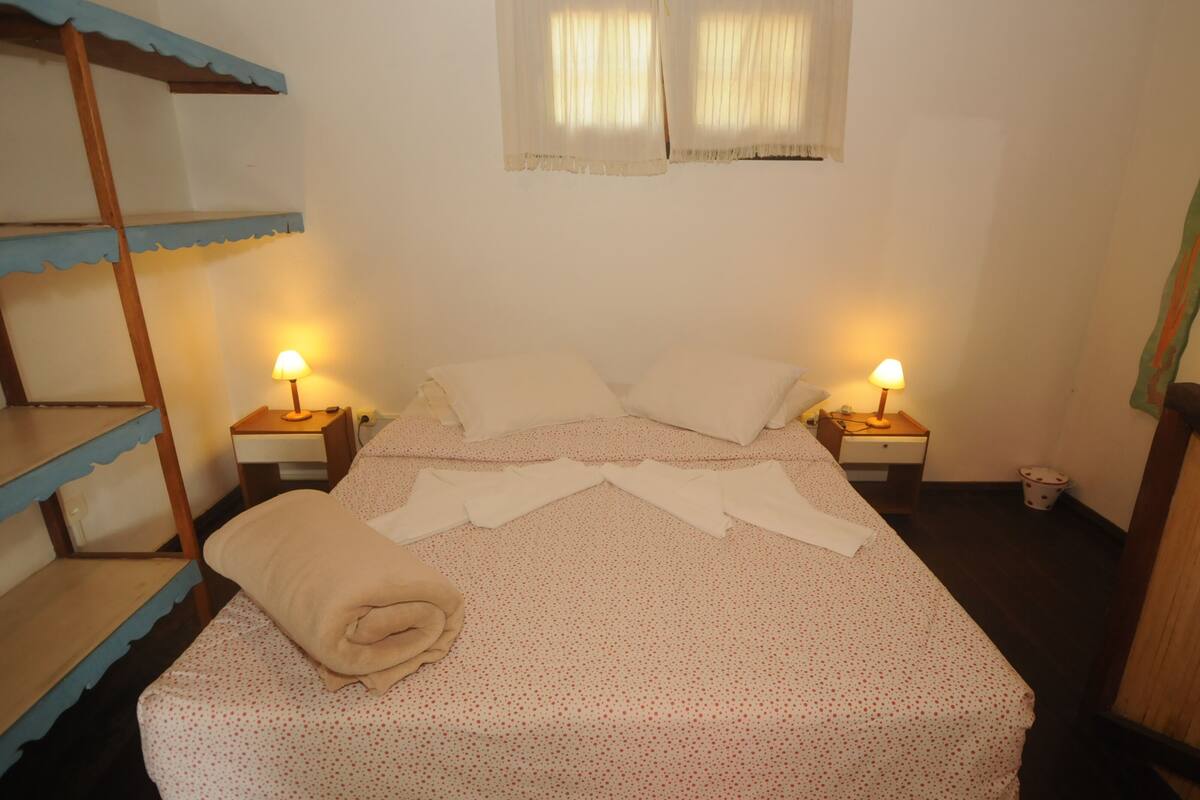 A single bed with a polka dot bedspread, two bedside lamps, a window with curtains, and a bunk bed to the left.