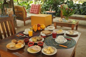 Une table de petit-déjeuner avec divers aliments, une cafetière et un panier de fruits.