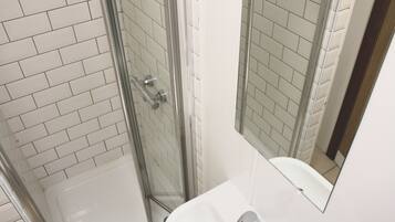 A bathroom with a glass shower enclosure, white tiles, and a sink with a mirror above it.