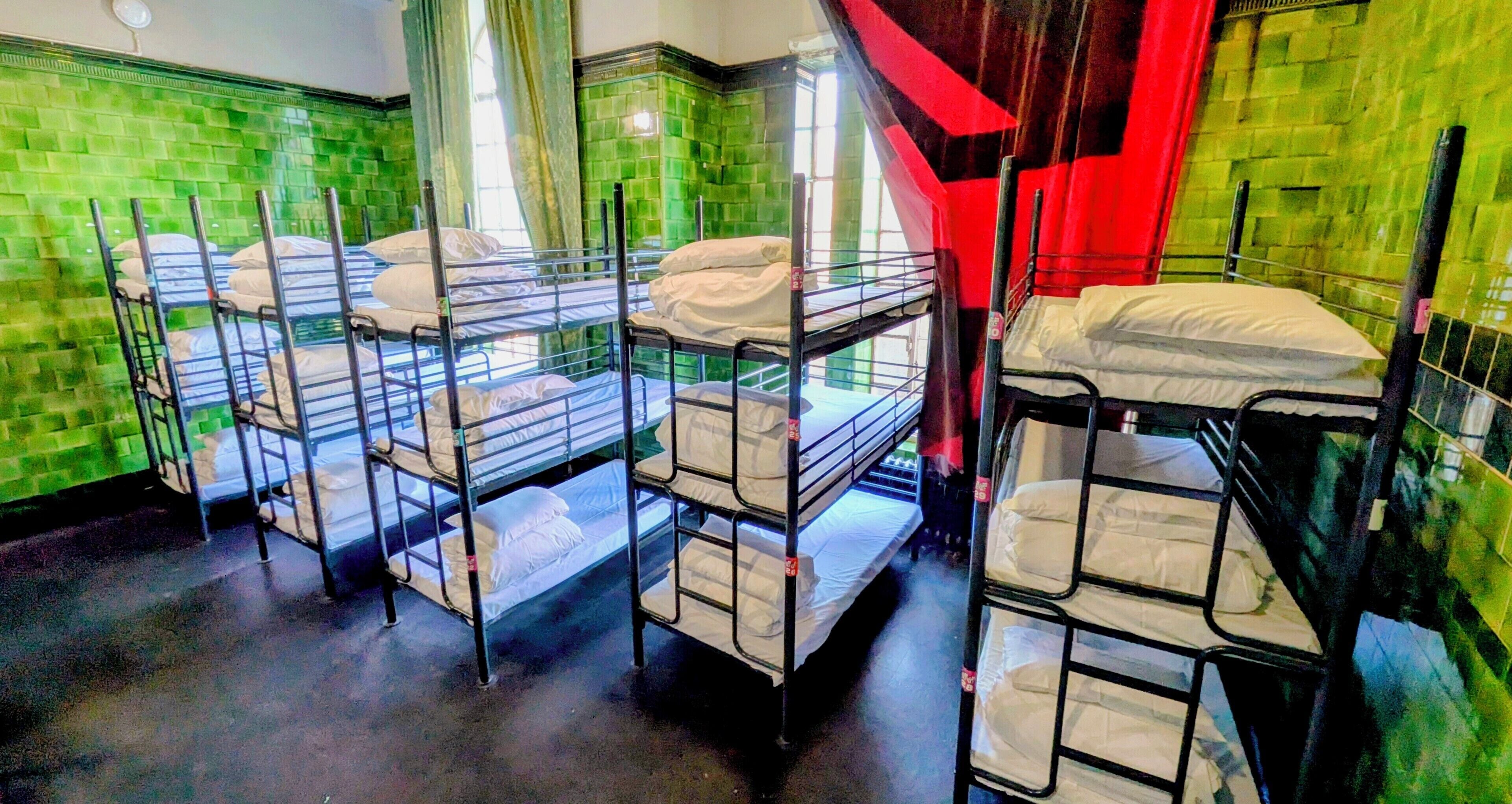 Bunk beds arranged in a room with green tiled walls and a staircase with red accents.