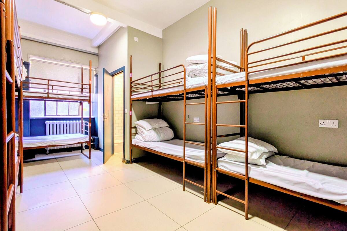 A dormitory room with bunk beds, a radiator, and a window.