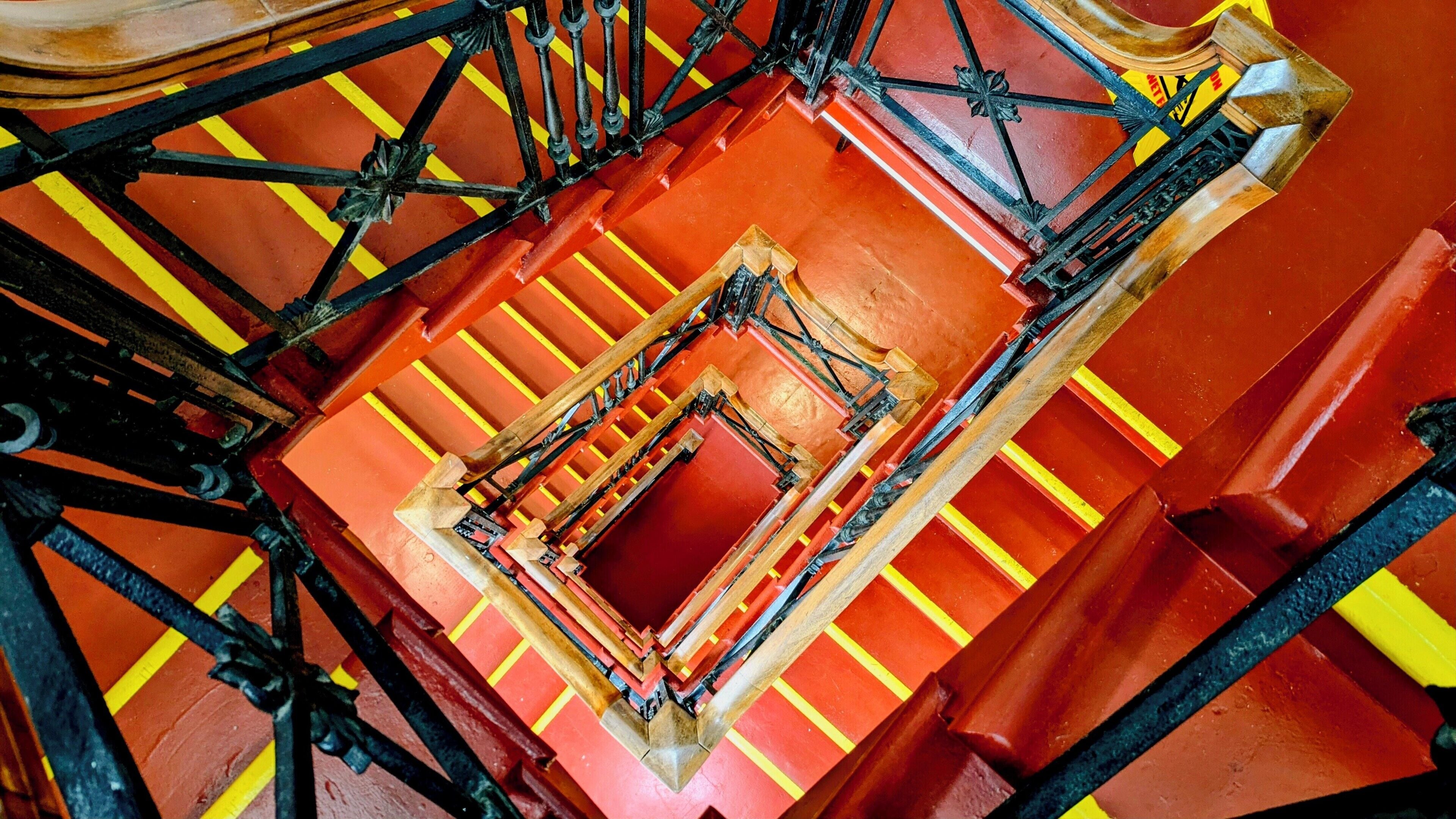 A spiral staircase with a red and yellow color scheme, metal railings, and a central wooden structure.