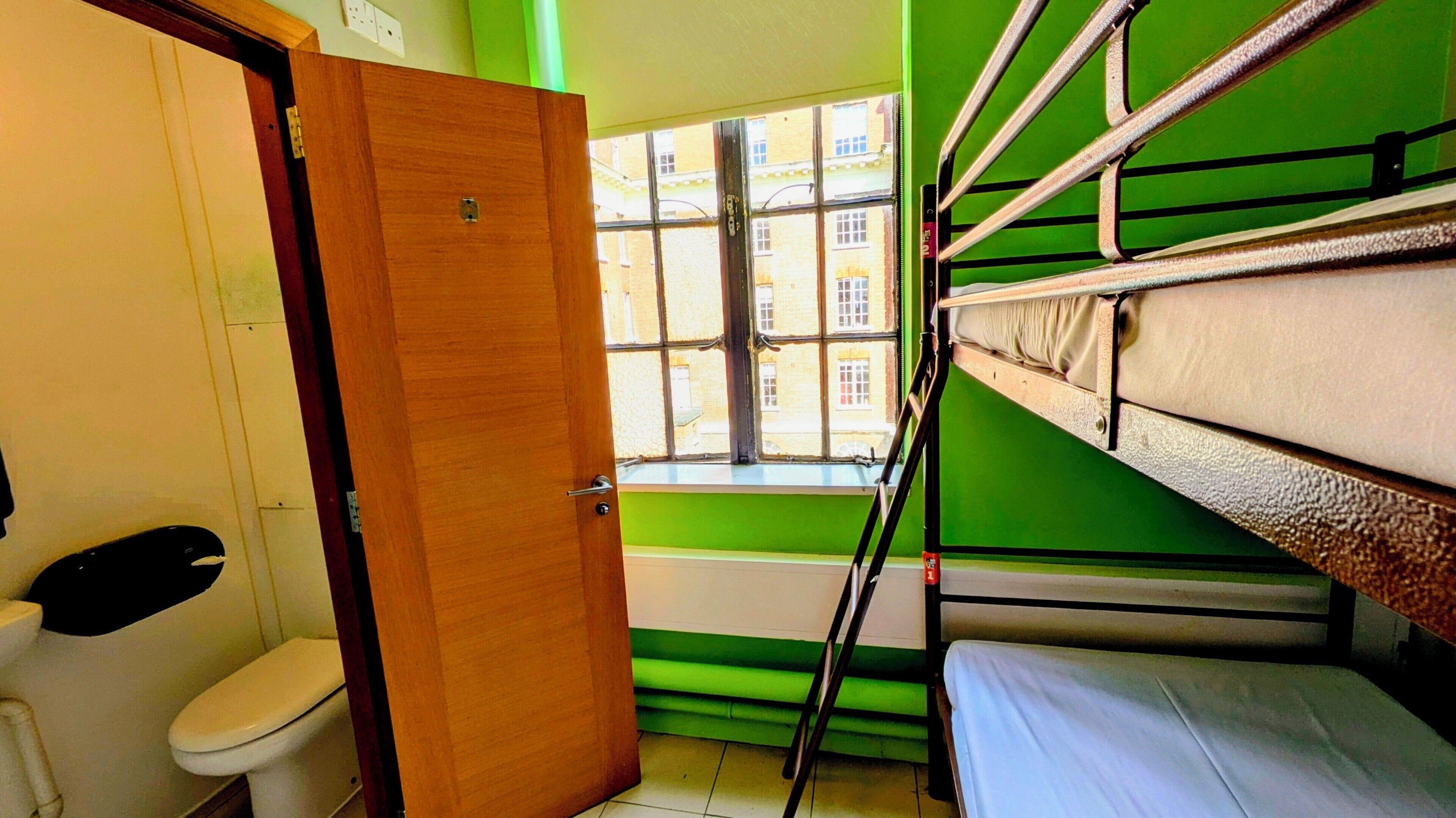 Ein Zimmer mit Etagenbetten, einer Toilette und einem Fenster mit Blick auf Gebäude.