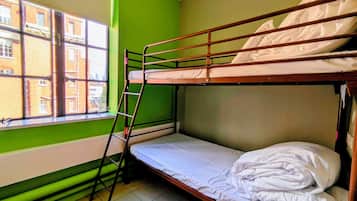 Een slaapkamer met stapelbed, raam en uitzicht op gebouwen.