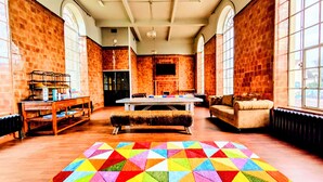 A spacious room with a large wooden table, a cushioned bench, and a colorful geometric rug. - Rest Up London - Hostel (London)