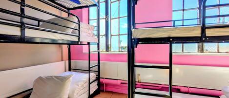 A bunk bed room with pink walls and a window.