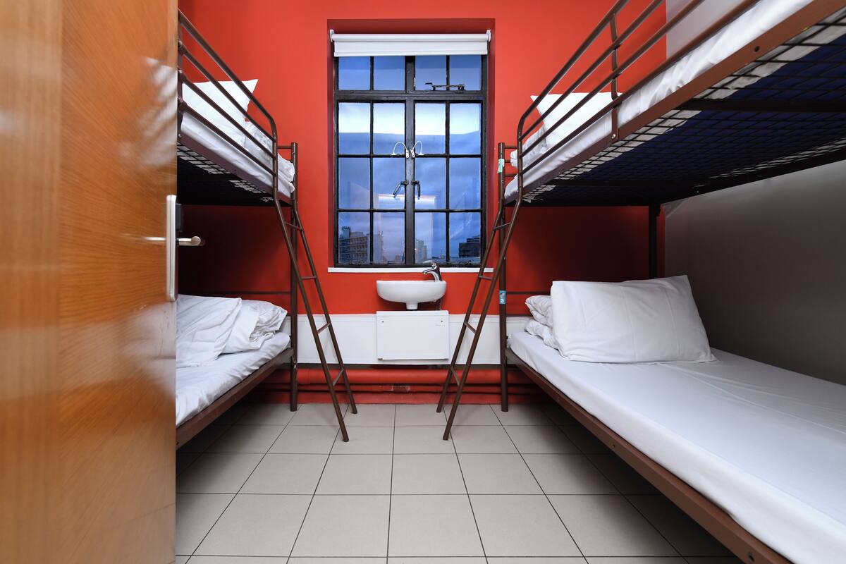 A dormitory room with bunk beds, a window, and a sink.