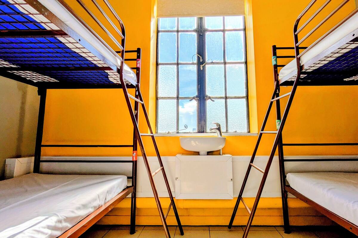 A dormitory room with bunk beds, a window, and a sink.