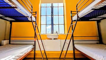 A dormitory room with bunk beds, a window, and a sink.