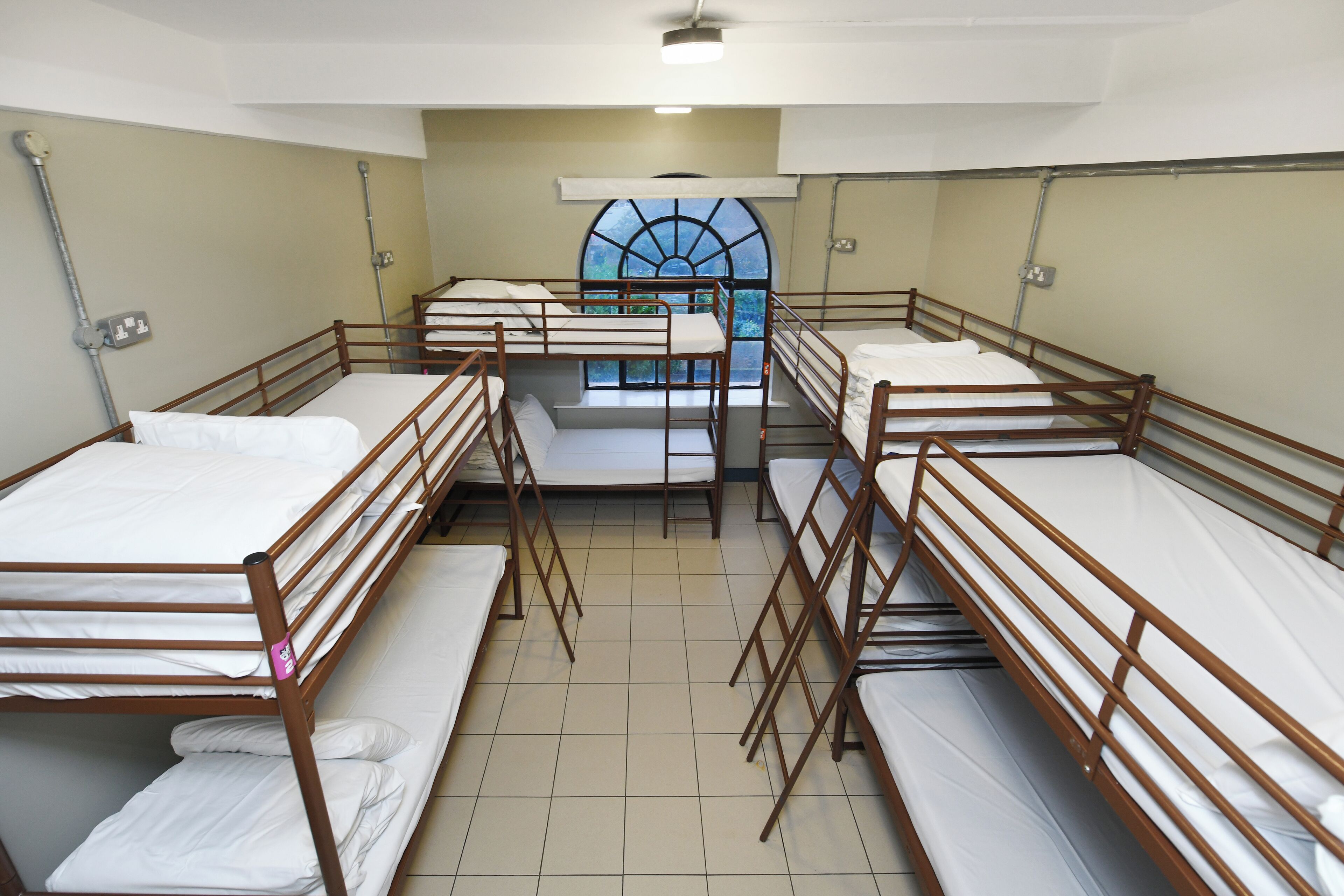 A dormitory room with bunk beds, a window with a view, and a ceiling fan.