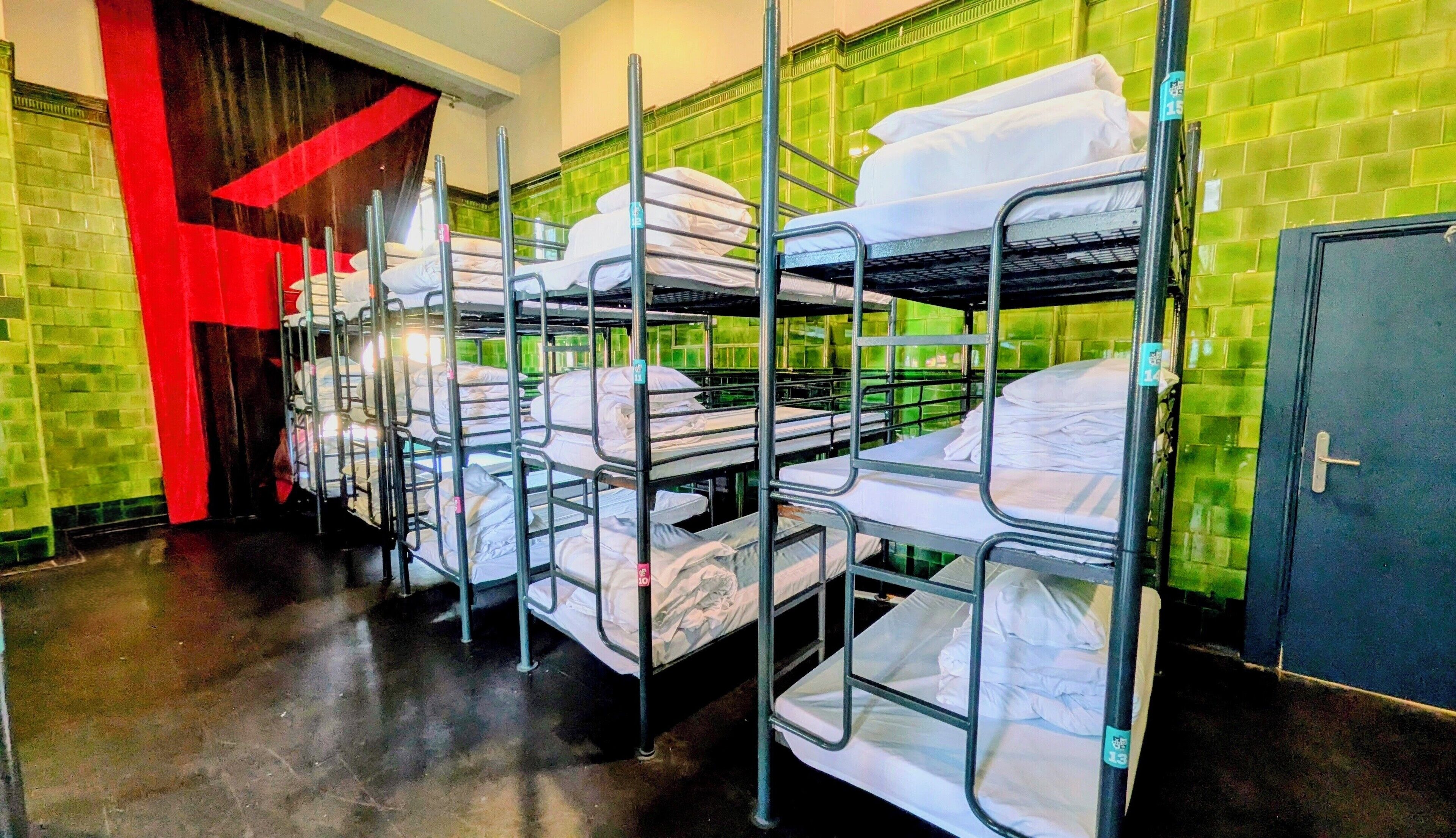 Bunk beds arranged in a dormitory-style room with green tiled walls and a red curtain.