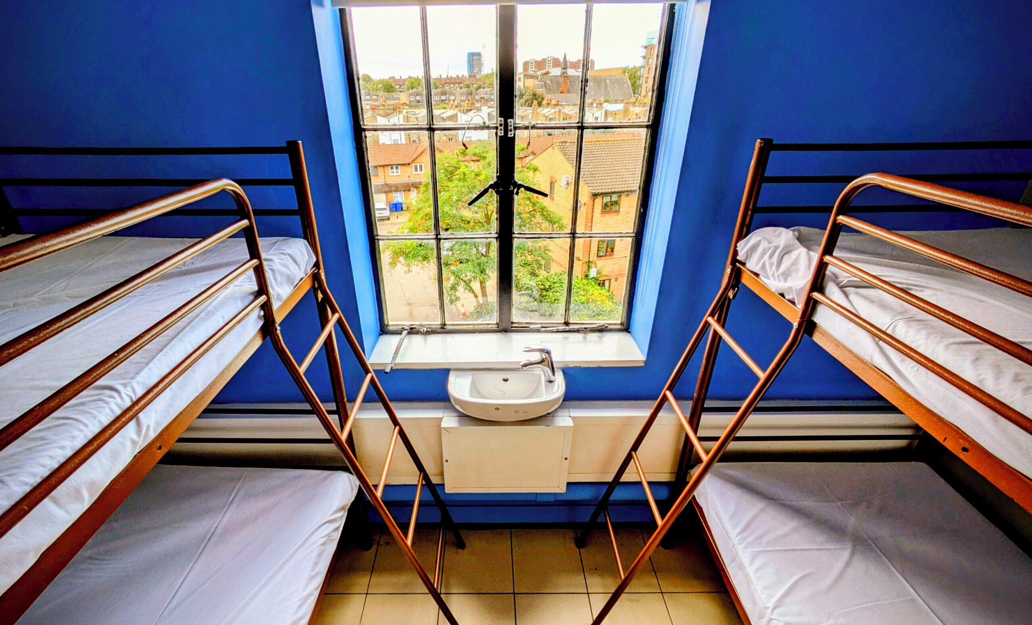 A dormitory room with bunk beds, a window with a view of buildings, and a sink.