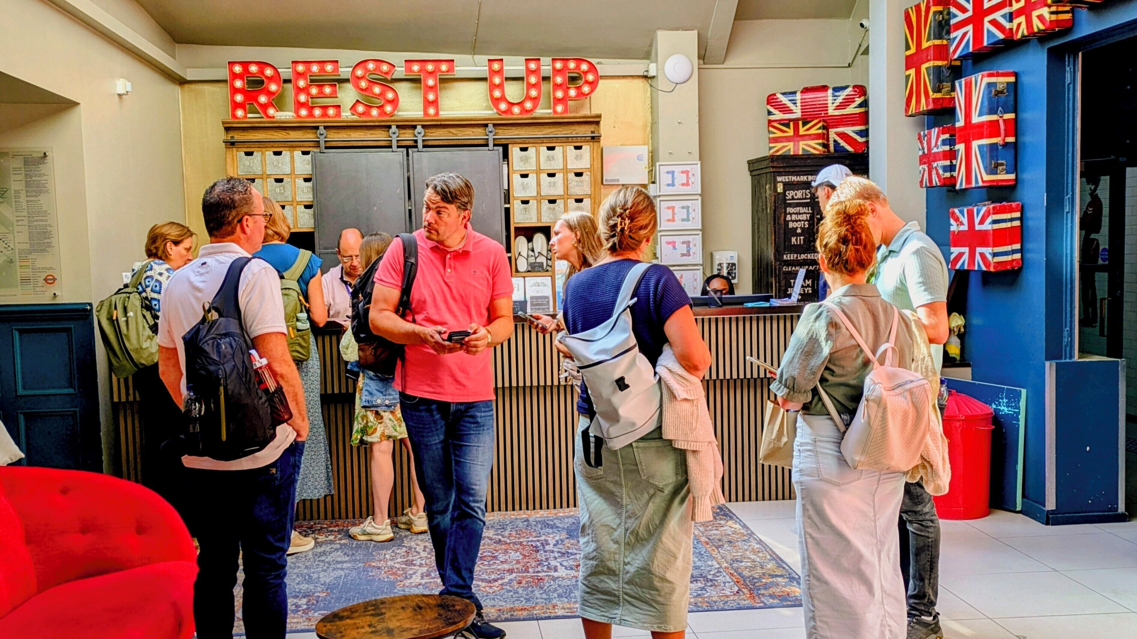 A group of people standing in front of a reception desk with a sign that reads "REST UP".